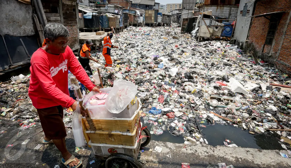 Pedagang melintas saat petugas mengangkut sampah yang menumpuk di Kali Gendong, Penjaringan, Jakarta, Kamis (16/3). Ceceran sampah plastik limbah rumah tangga terlihat menyerupai daratan menumpuk di sepanjang Kali Gendong. (Liputan6.com/Faizal Fanani)