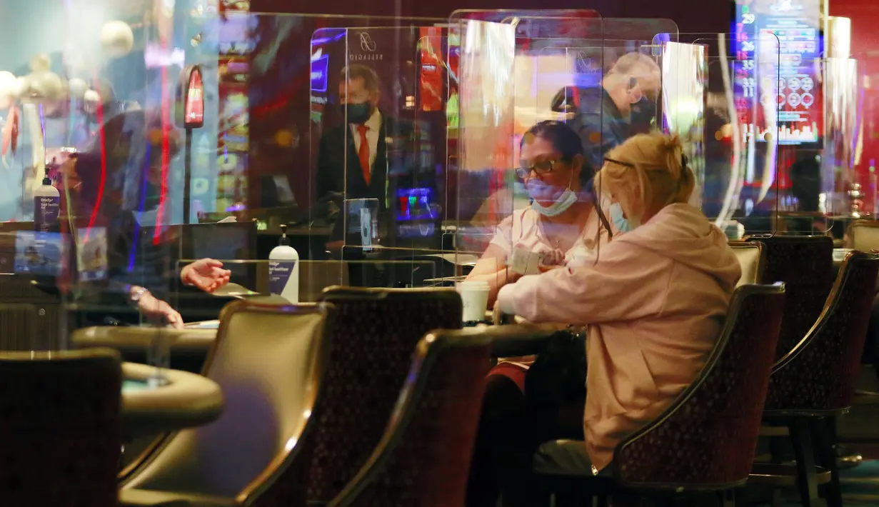Pemain dan pekerja meja permainan dipisahkan oleh plexiglass saat pembukaan kembali hotel dan kasino Bellagio, Las Vegas, Nevada, Amerika Serikat, Kamis (4/6/2020). Kasino di Nevada diizinkan kembali beroperasi setelah penutupan sementara untuk mencegah penyebaran COVID-19. (Ronda Churchill/AFP)