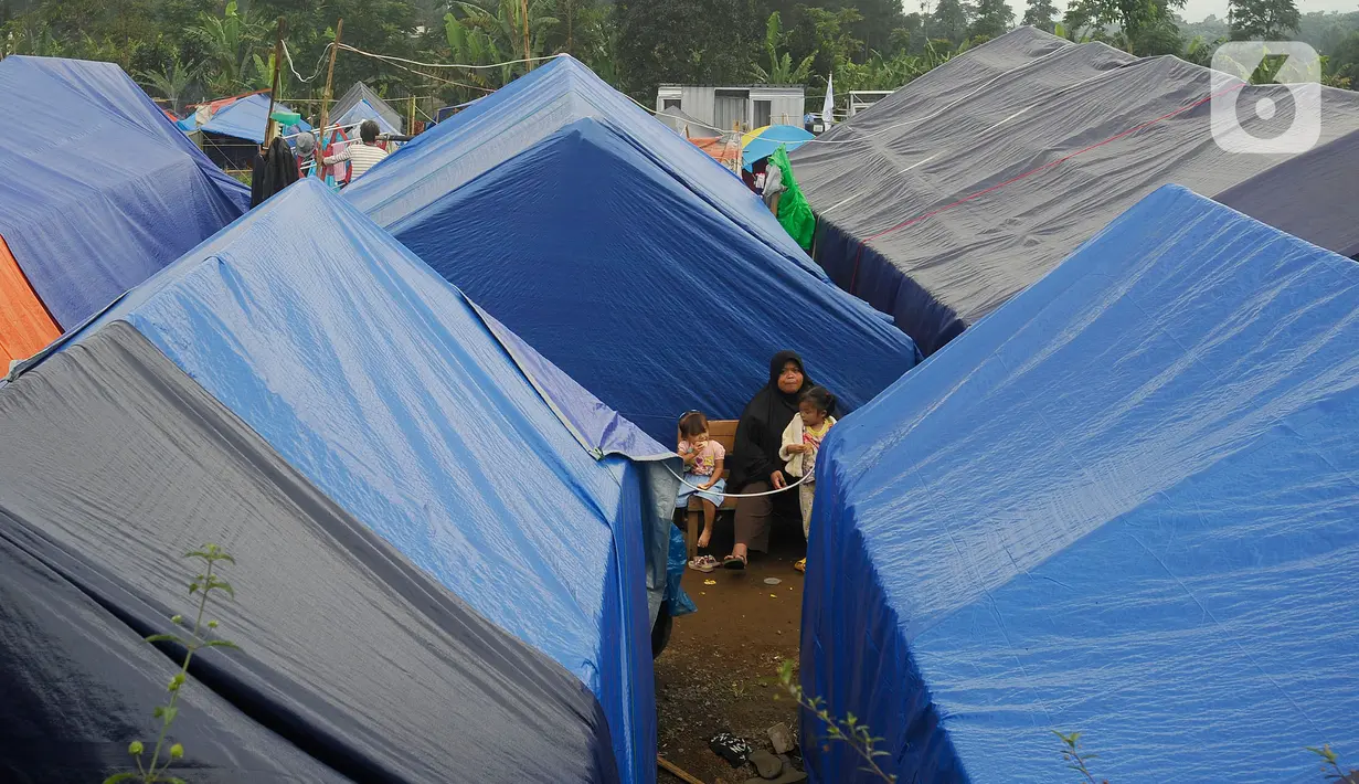 Warga duduk diantara hunian sementara penyintas  gempa di Desa Kramat, Cianjur, Jumat (23/12/2022). Lebih dari sebulan sejak musibah gempa bumi 5,2 SR sejumlah warga masih tinggal di pengungsian dan hunian sementara dengan bantuan kebutuhan hidup dari para donatur. (merdeka.com/Arie Basuki)