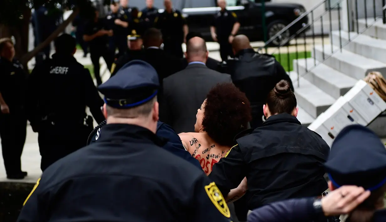 Polisi menggelandang pengunjuk rasa wanita yang tampil topless di sidang kekerasan seksual komedian Bill Cosby, Pennsylvania, AS, Senin (9/4). (AP Photo/Corey Perrine)