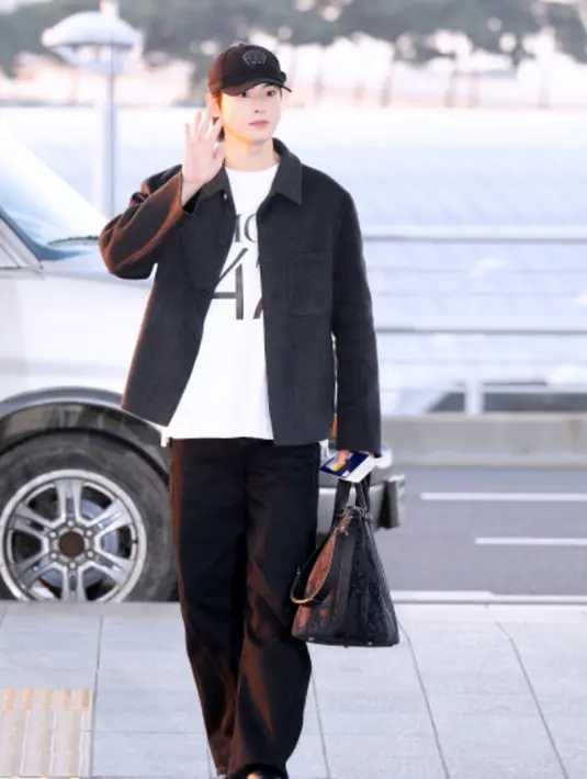 Saat di bandara, Cha Eunwoo tampil dengan jaket hitam serasi dengan celana, tad, topi, dan bootsnya. Dipadukan tshirt putih sebagai inner. [Dior]