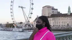 Seorang wanita yang mengenakan masker berjalan di Jembatan Westminster dengan latar pemandangan London Eye di London, Inggris (31/10/2020). Kasus baru COVID-19 di Inggris mencapai 21.915, menambah total kasus coronavirus di negara itu menjadi 1.011.660. (Xinhua/Han Yan)