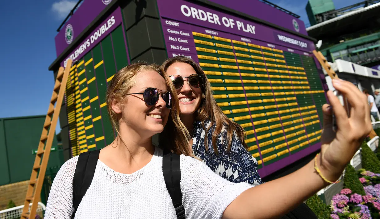 Dua wanita berselfie di sebelah papan Order of Play pada hari ketiga Kejuaraan Tenis Wimbledon 2017 di The All England Lawn Tennis Club di Wimbledon, London barat daya, Inggris (5/7). (AFP Photo/Justin Tallis)
