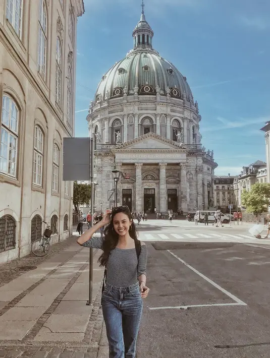 Wanita kelahiran tahun 1995 ini mengembangkan senyumnya saat berjalan di jalanan Copenhagen. Menggunakan baju kaus dan celana jeans, Anggika berpose di depan sebuah bangunan ikonik di sana. (Liputan6.com/IG/@anggikabolsterli)