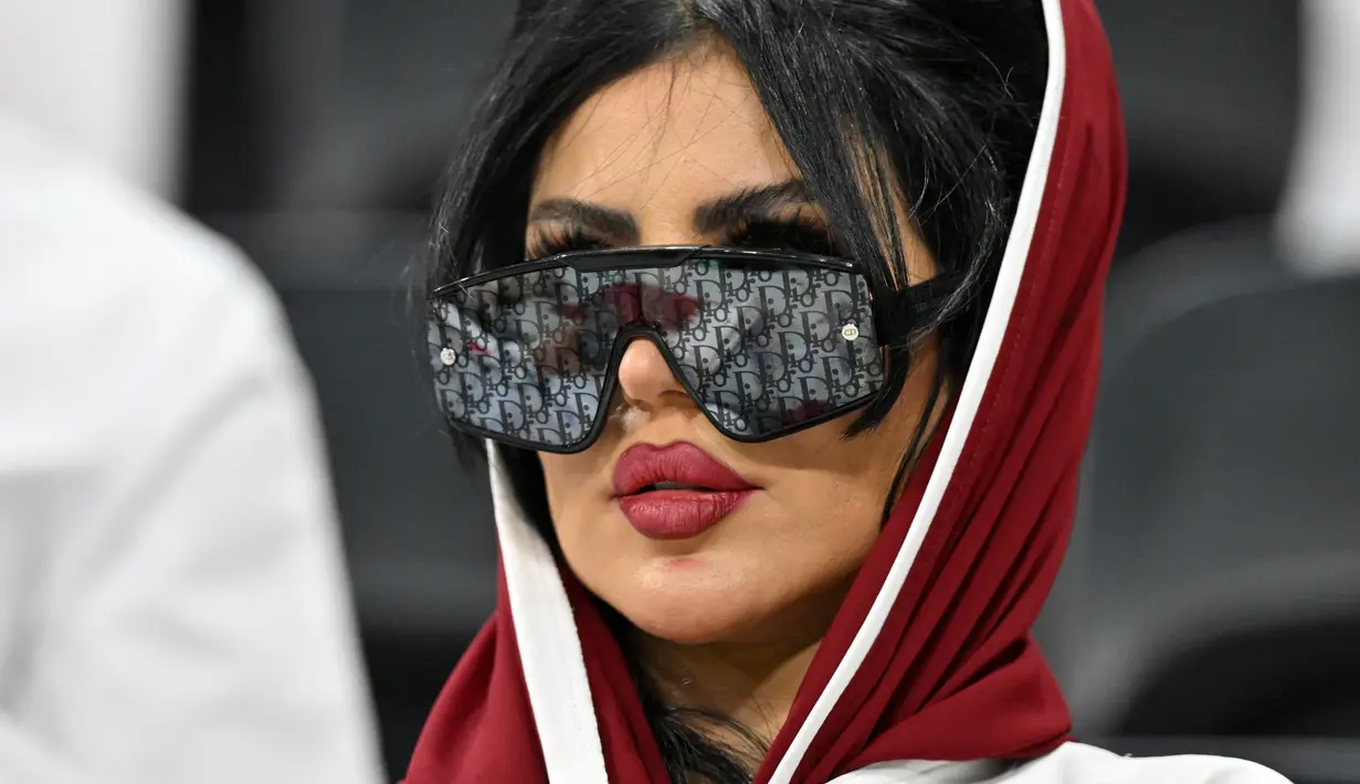 <p>Seorang wanita pendukung Qatar mengenakan kaca mata hitam menghadiri pertandingan Grup A Piala Dunia Qatar 2022 antara Qatar dan Ekuador di Stadion Al-Bayt di Al Khor, utara Doha pada 20 November 2022. (AFP/Glyn Kirk)</p>