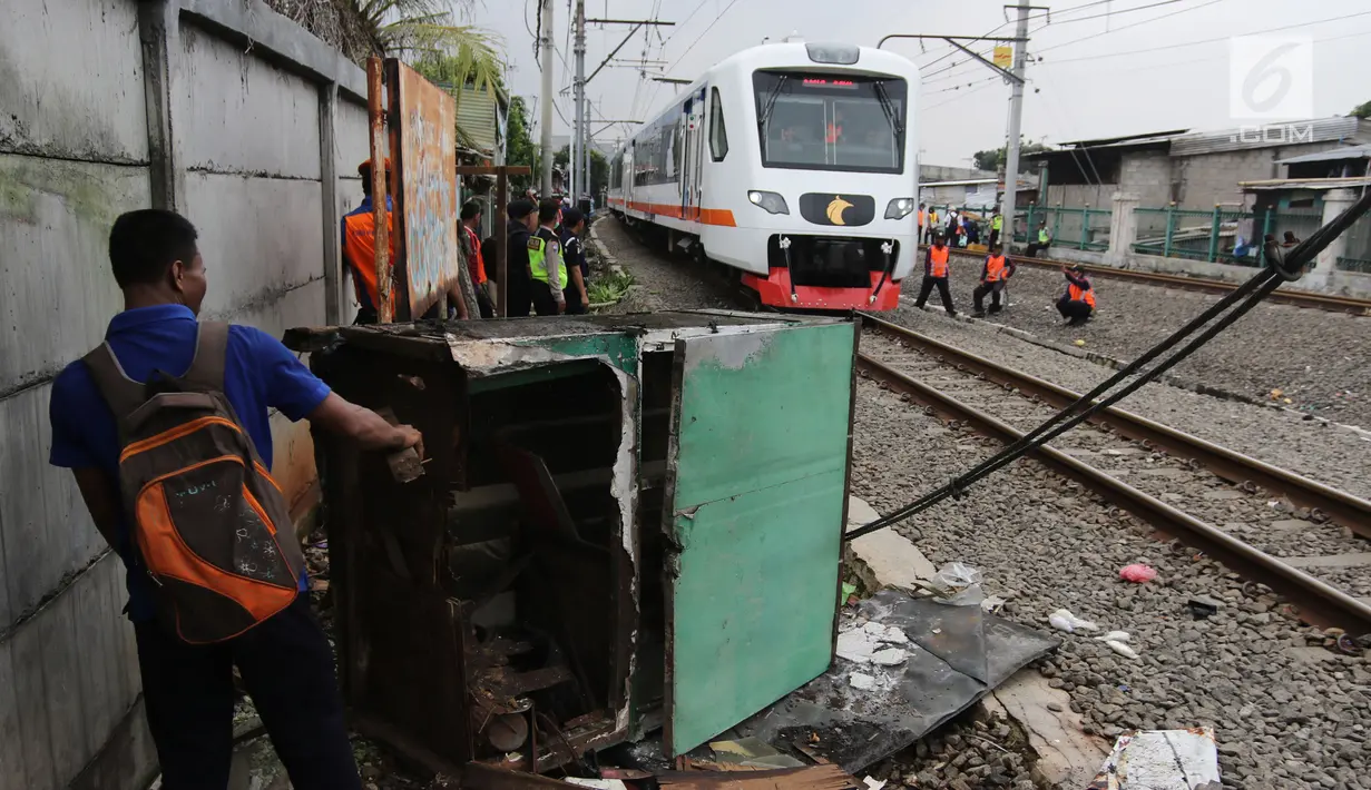 Kereta bandara melintas di dekat petugas yang sedang melakukan penertiban lapak dan bangunan liar di sepanjang jalur kereta di kawasan Grogol, Jakarta Barat, Kamis (22/2). (Liputan6.com/Arya Manggala)