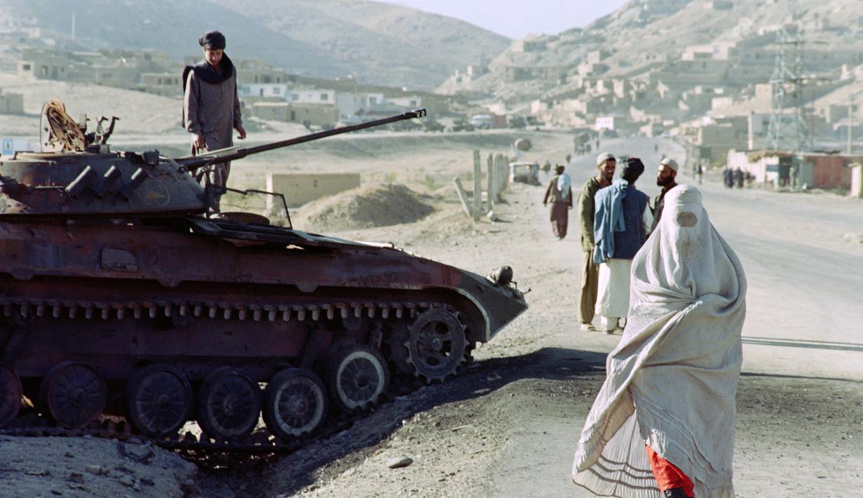 Seorang wanita mengenakan burqa yang diwajibkan Taliban saat melarikan diri ke Kabul dari daerah garis depan melewati kendaraan lapis baja milik mantan pasukan pemerintah di Kabul, Afghanistan, 30 Oktober 1996. (SAEED KHAN/AFP)