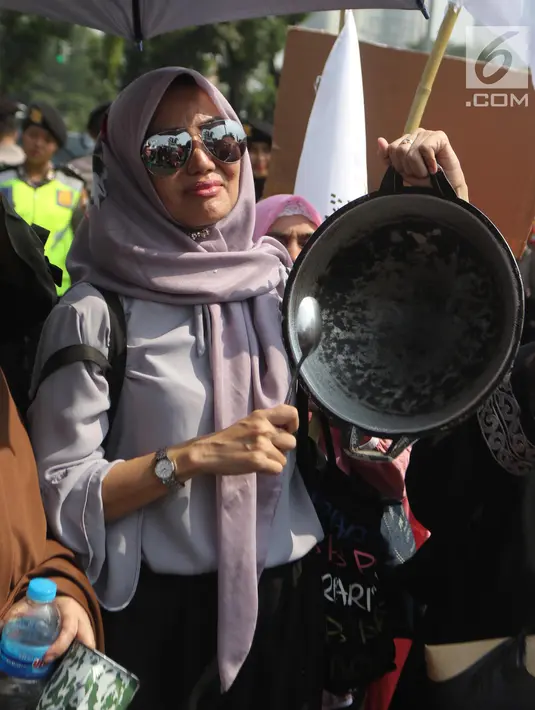 Seorang ibu dari Barisan Emak-Emak Militan Indonesia membawa wajan saat menggelar aksi di seberang Istana Merdeka, Jakarta, Rabu (18/7). Dalam aksinya, emak-emak ini  membawa peralatan memasak seperti penggorengan dan panci. (Liputan6.com/Arya Manggala)