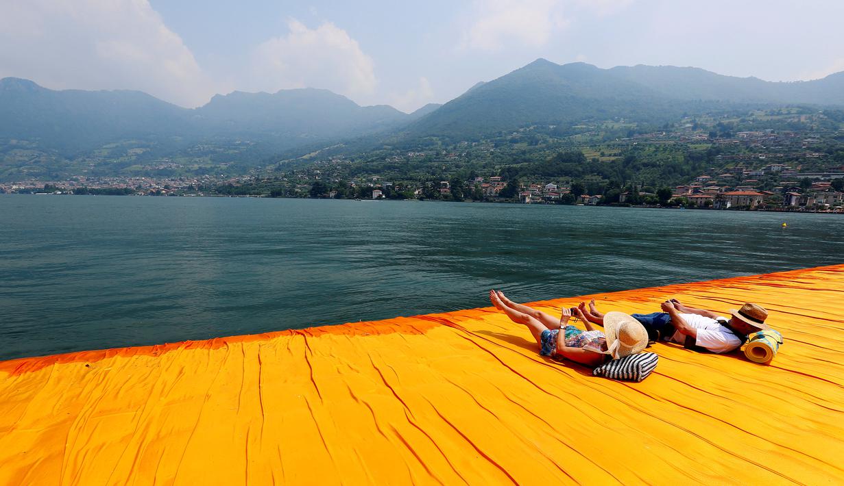 Dua wisatawan bersantai di atas seni instalasi 'The Floating Piers' sambil melihat landscape pemandangan bukti dan pegunungan di utara Italia karya Christo Vladimirov Javacheff di Danau Iseo, Italia utara, (24/6). (REUTERS/Stefano Rellandini)