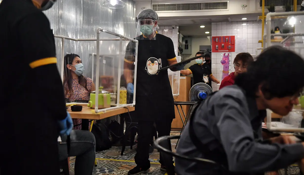 Pramusaji dengan pelindung wajah melayani pelanggan di restoran hotpot Penguin Eat Shabu di Bangkok, 5 Mei 2020. Restoran yang memasang pembatas plastik itu kembali dibuka setelah Thailand memperlonggar lockdown dengan mengizinkan tempat makan menerapkan social distancing. (Lillian SUWANRUMPHA/AFP)