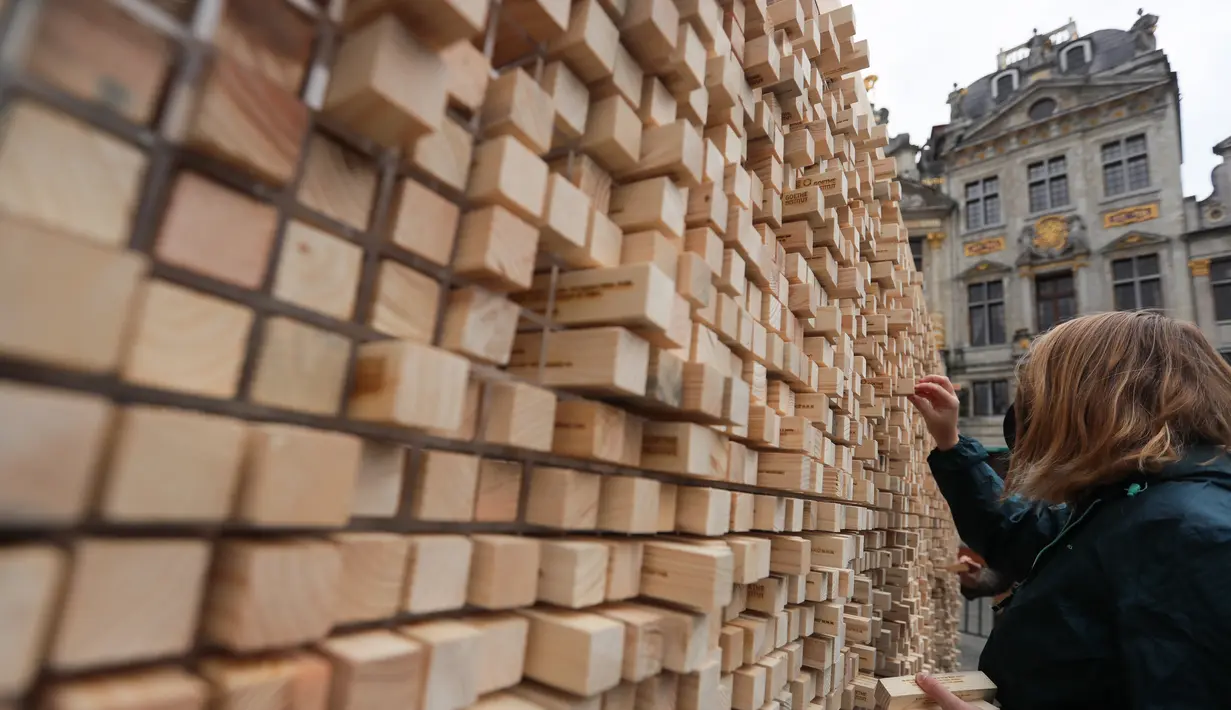 Seorang perempuan mengambil sejumlah balok kayu dari " The Disappearing Wall" di Grand Place, Brussel, Belgia, 3 Oktober 2020. Instalasi seni memperingati 30 tahun reunifikasi Jerman itu terdiri dari 6.000 balok kayu dilengkapi kutipan seniman dan pemikir dari seluruh dunia. (Xinhua/Zheng Huansong)