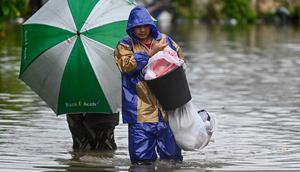 Kesembilan daerah terdampak itu adalah Bireuen, Lhokseumawe, Aceh Utara, Aceh Timur, Bener Meriah, Aceh Singkil, Gayo Lues, Aceh Selatan, dan Langsa. Tampak dalam foto, seorang pria dan seorang wanita membawa barang-barang mereka saat mengarungi banjir di jalan yang tergenang akibat hujan deras di permukiman Darul Imarah di pinggiran Banda Aceh pada Kamis 27 November 2025. (CHAIDEER MAHYUDDIN/AFP)