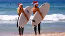  Dua wisatawan asal Jerman mengenakan topi Natal bersiap bermain surfing di Bondi Beach Sydney pada Hari Natal di Australia, (25/12). (REUTERS/David Gray)