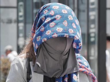Seorang pejalan kaki mengenakan kain di atas kepalanya untuk melindungi diri dari panas dan terik matahari di Tokyo pada 5 Agustus 2025. (Kazuhiro NOGI/AFP)