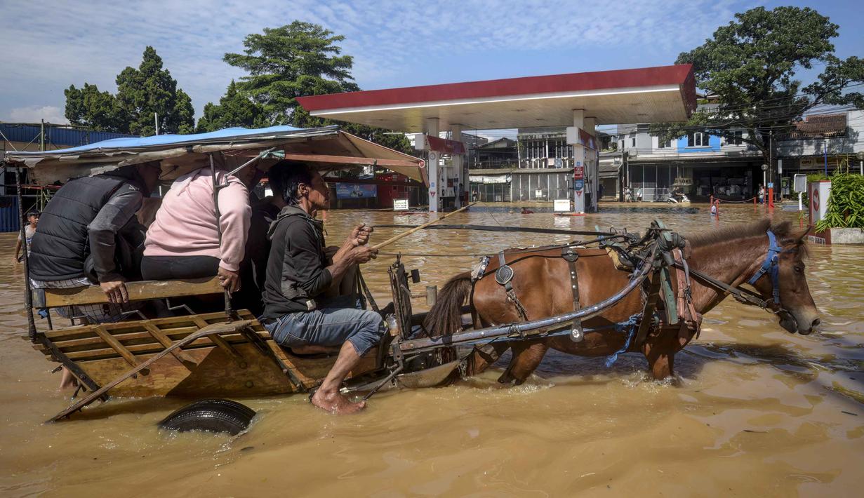 Sebuah kereta kuda mengangkut penumpang melewati jalan yang tergenang banjir melewati sebuah Stasiun Pengisian Bahan Bakar Umum (SPBU) di Bandung, Jawa Barat pada Jumat 5 Desember 2025. Banjir melanda berbagai wilayah di Kabupaten Bandung. Curah hujan tinggi pada Kamis (4/12/2025) sore hari, mengakibatkan aliran sungai Citarum meluap dan merendam sejumlah pemukiman hingga hari ini. (TIMUR MATAHARI/AFP)