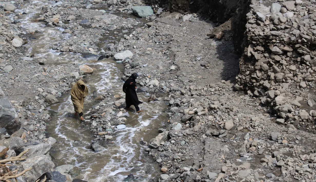 Seorang wanita menyebrangi sungai setelah jalanan rusak akibat banjir bandang di Ursoon, daerah terpencil Chitral di Pakistan utara, Minggu (3/7). Banjir merusak sejumlah rumah dan sebuah masjid dengan jumlah korban tewas 43 orang (GUL HAMAAD Farooqi/AFP)