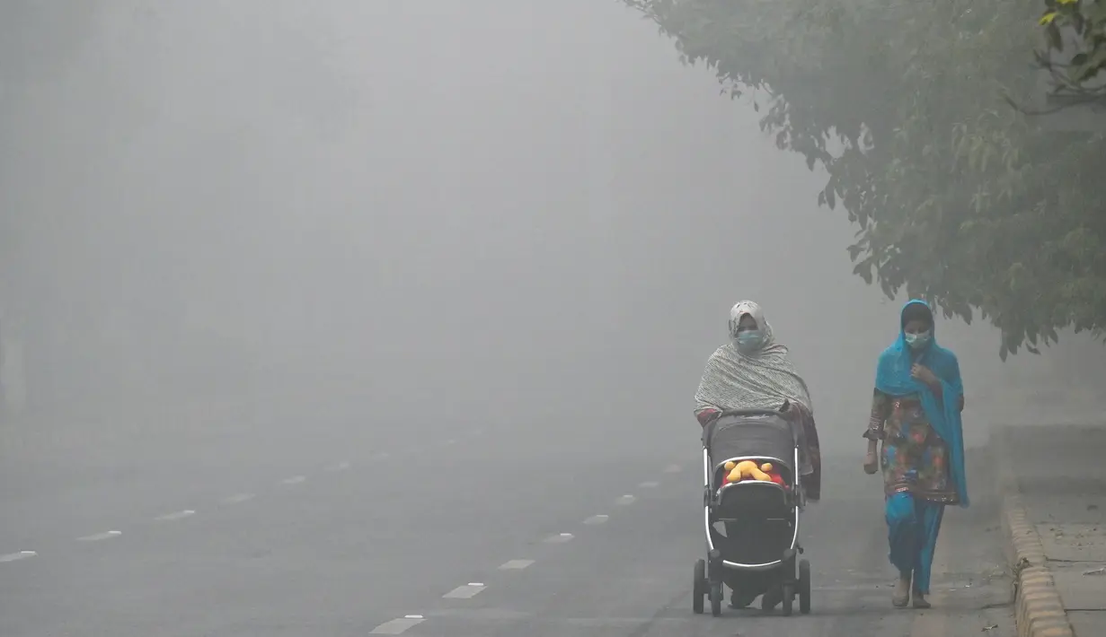 Seorang wanita berjalan di sepanjang jalan yang diselimuti kabut asap di Lahore pada Kamis 14 November 2024. (Arif ALI/AFP)