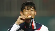 Penyerang Korea Selatan, Son Heung-min, menggigit mendali, usai menjuarai Asian Games dengan mengalahkan Jepang di Stadion Pakansari, Jawa Barat, Sabtu (1/9/2018). (AP/Bernat Armangue)