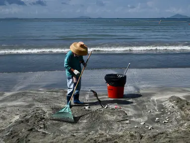 Seorang pria membersihkan sisa tumpahan minyak sawit dari pasir di sebuah pantai di Hong Kong, Senin (7/8). Sepuluh pantai di Hong Kong ditutup pada Minggu (6/8) setelah minyak sawit tumpah akibat tabrakan kapal di perairan China. (Anthony WALLACE / AFP)