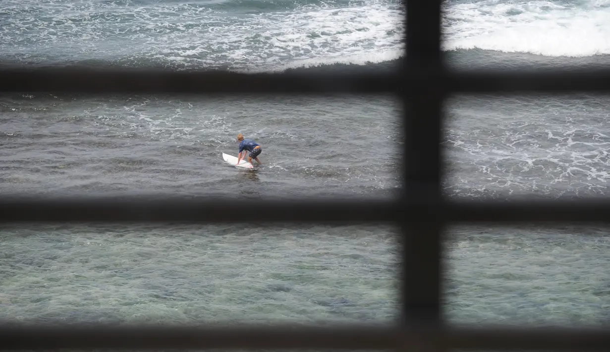 Seorang turis bersiap untuk bermain selancar di pantai Uluwatu Kuta Selatan di Kabupaten Badung, Bali pada 20 Desember 2018. Jutaan turis mancanegara datang ke Bali untuk berburu spot berselancar paling menantang. (Photo by SONNY TUMBELAKA / AFP)