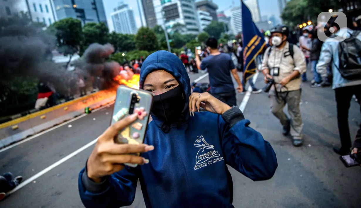 Pendemo berselfie di kobaran api saat aksi unjuk rasa di kawasan patung kuda, Jakarta, Selasa (20/10/2020). Gelombang protes tolak UU Cipta Kerja belum surut sejak disahkan pada 5 Oktober lalu. (Liputan6.com/Faizal Fanani)