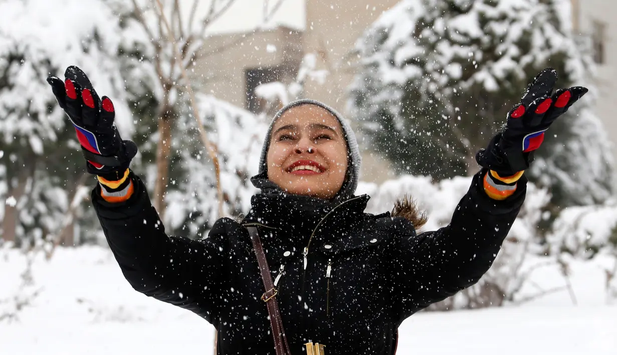 Seorang wanita melempar salju di Teheran, Selasa (24/1). Hampir setengah abad salju tak turun di Iran dan sejak 2011 hingga kini salju senantiasa turun di musim dingin. (AFP PHOTO / ATTA KENARE)   