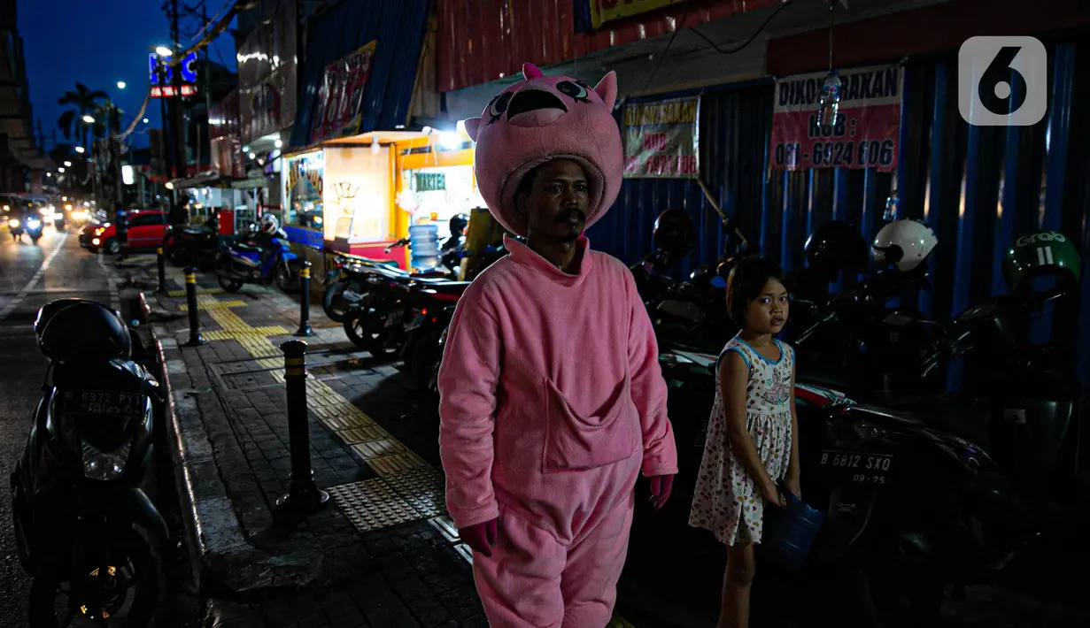 Warkuatno (41) bersama anak sulungnya, Bunga (9) berjalan kaki di pinggir Jalan Raya Fatmawati, Jakarta, Rabu (6/1/2021). Mantan sopir Metromini 75 ini menjadi badut keliling sejak bulan Maret lalu, tak lama setelah kasus corona COVID-19 terdeteksi di Indonesia. (Liputan6.com/Faizal Fanani)