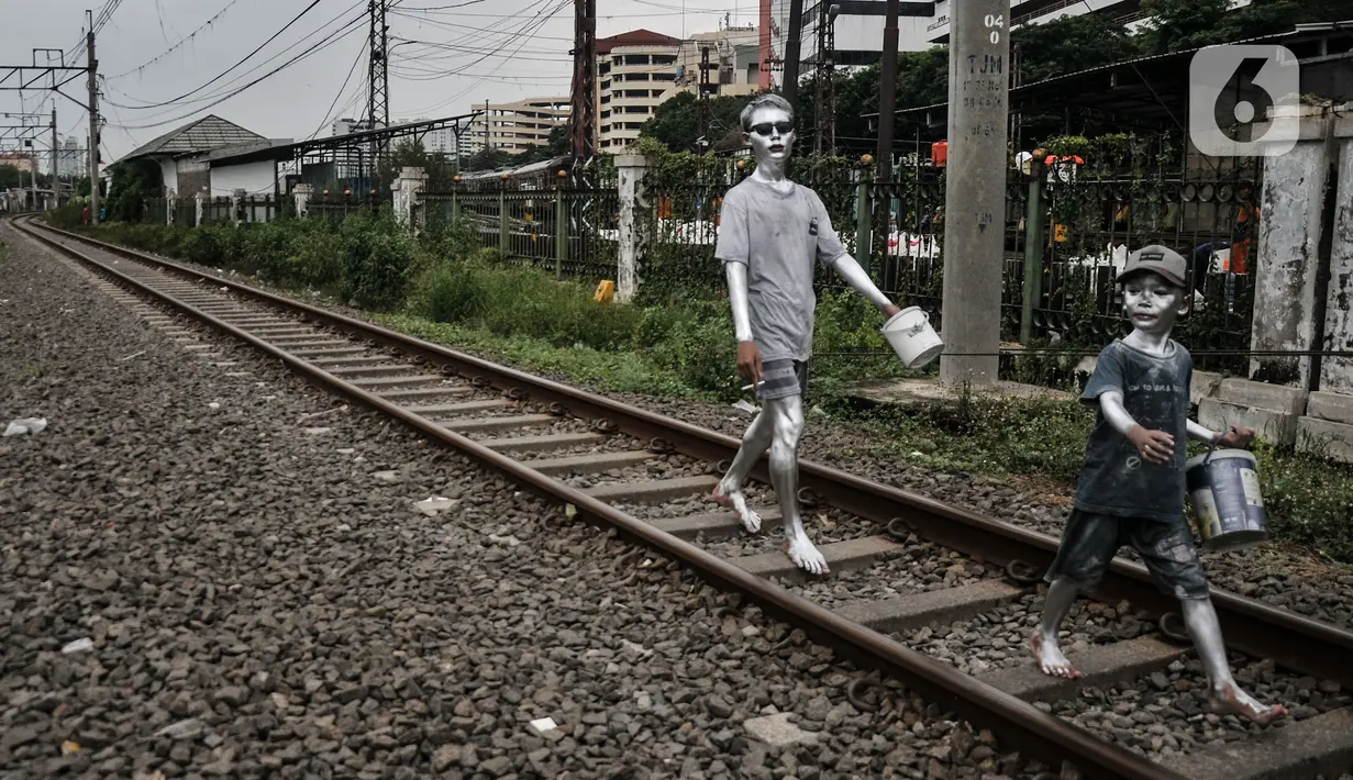 Anak-anak 'Manusia Silver' saat melintasi rel kereta di kawasan Pademangan, Jakarta Utara, Kamis (16/3/2023). (merdeka.com/Iqbal S Nugroho)