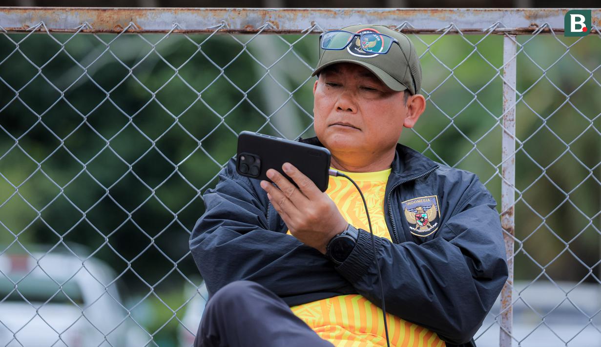 Manajer Timnas Indonesia U-22, Sumardji, tampak serius menyaksikan laga Timnas Vietnam U-22 vs Timnas Malaysia U-22 dari layar handphone. (Bola.com/Bagaskara Lazuardi)