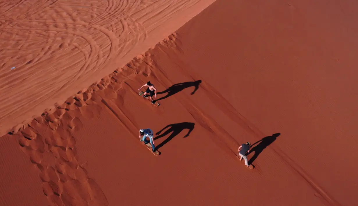 Sejumlah turis mencoba atraksi berseluncur dengan sandboarding di gurun Dubai pada 11 Januari 2021. Di sini para wisatawan dapat mencoba sensasi bermain sandboarding sambil memandang hamparan lautan pasir cokelat. (Photo by GIUSEPPE CACACE / AFP)