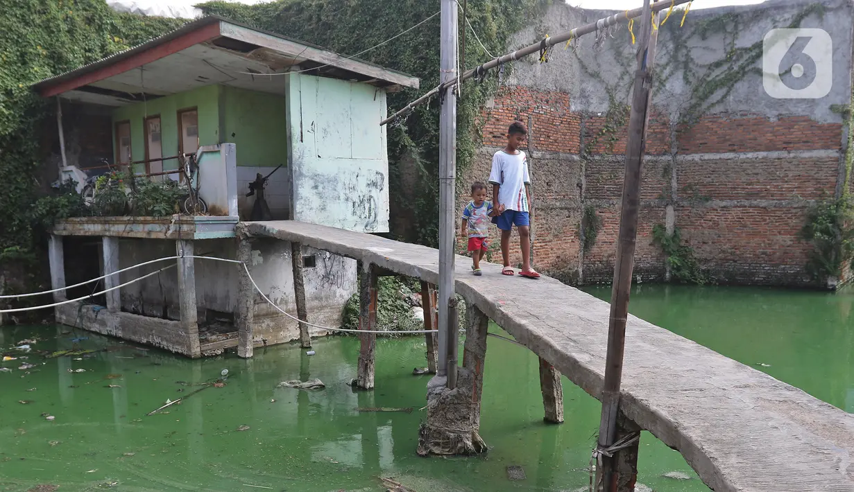 Dua orang anak melintas di Kampung Apung, Jakarta, Selasa (26/11/2019). Untuk mengurangi genangan air di Kampung Apung, Pemprov DKI berencana membuat saluran air pada 2020 mendatang, selain itu akan disediakan beberapa pompa mobile saat musim hujan tiba. (Liputan6.com/Herman Zakharia)