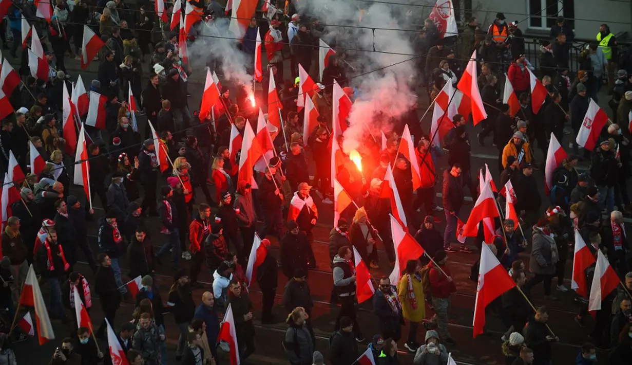 Orang-orang mengibarkan bendera nasional Polandia saat pawai untuk menandai Hari Kemerdekaan Nasional Polandia di Warsawa, Polandia, 11 November 2021. Hari Kemerdekaan Nasional Polandia dirayakan pada 11 November untuk memperingati ulang tahun Republik Polandia Kedua. (Adam Chelstowski/AFP)