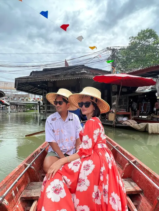 Ririn Ekawati bersama suami saat mengunjungi sebuah kampung terapung dengan menggunakan perahu. Ririn tampil cantik mengenakan busana berwarna merah motif kembang dan topi di kepalanya. (Instagram/ririnekawati)