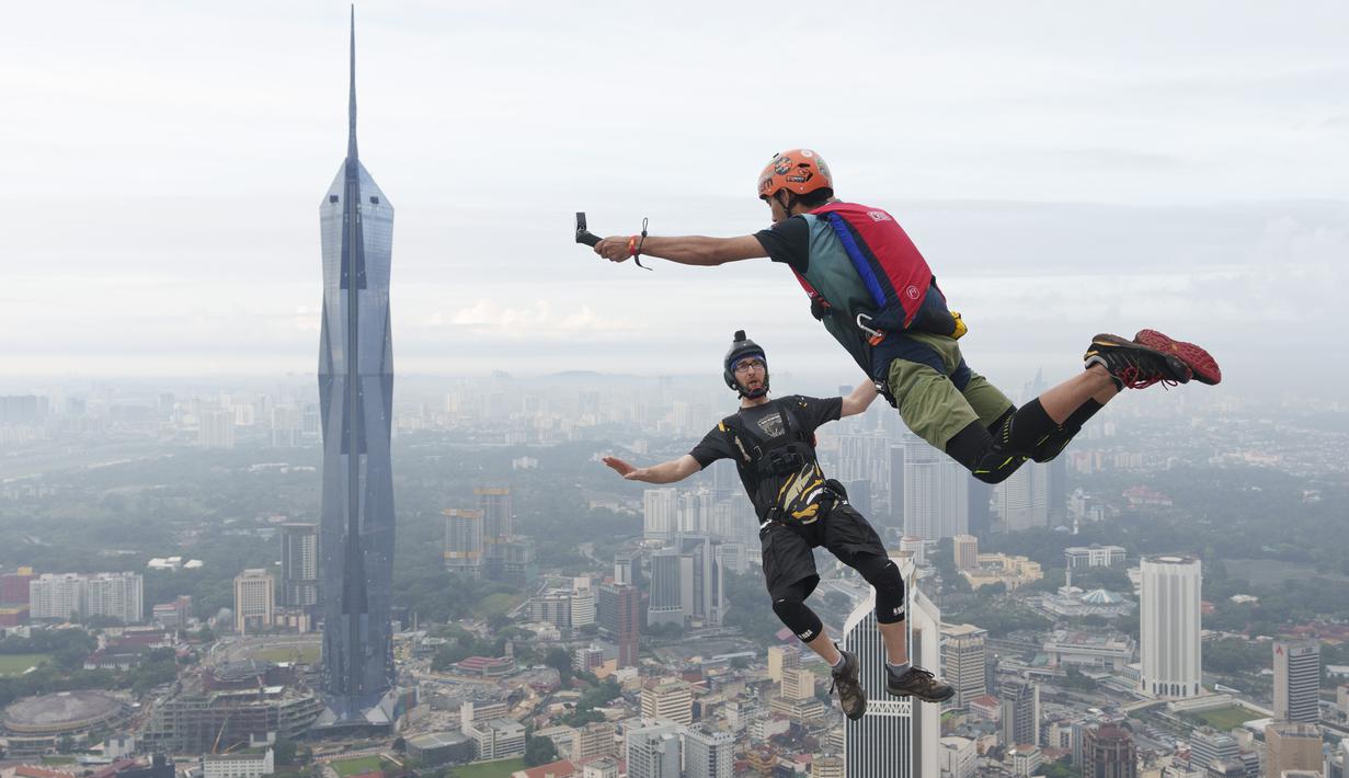 Sepasang pelompat BASE terjun dari Menara Kuala Lumpur selama KL Tower International Jump Malaysia di Kuala Lumpur, Jumat (3/2/2023). Satu persatu peserta pemberani, ada juga yang sekaligus berdua, meloncat sambil membawa parasut masing-masing. (AP Photo/Vincent Thian)