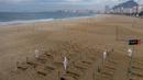 Aktivis LSM Rio de Paz menggali kuburan sebagai bentuk protes di pantai Copacabana, Rio de Janeiro, Kamis (11/6/2020). Kuburan-kuburan dengan simbol salib hitam yang dihiasi bendera Brasil kecil itu untuk mengenang puluhan ribu pasien corona yang meninggal di negara tersebut. (AP Photo/Leo Correa)