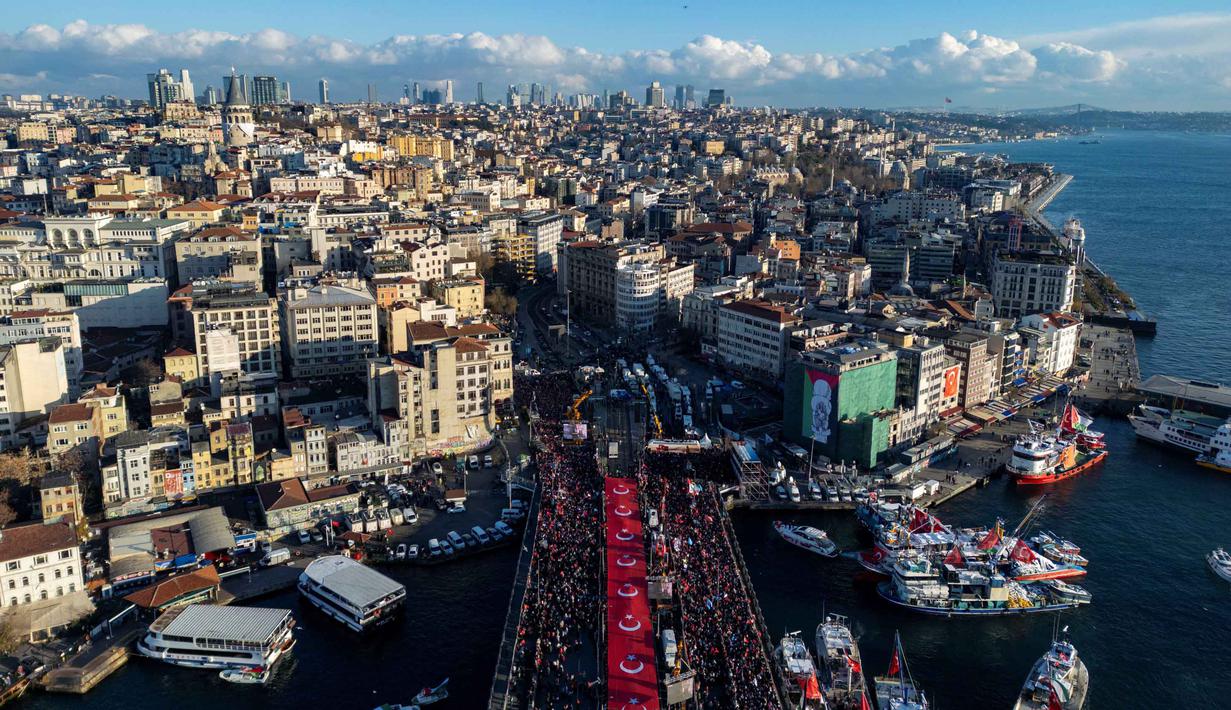 Tidak sedikit warga Palestina di Gaza memilih berteduh di bangunan yang rusak parah akibat serangan Israel, meski berisiko runtuh. Tampak foto udara menunjukkan ribuan orang yang berdemonstrasi menunjukkan solidaritas mereka dengan rakyat Palestina di tengah perang yang sedang berlangsung antara Israel dan kelompok Hamas di wilayah Gaza, di Jembatan Galata, Istanbul, Turki pada 1 Januari 2026. (Yasin AKGUL/AFP)