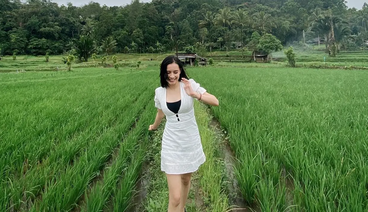 Tak perlu jauh, menikmati alam juga bisa di pematang sawah. Hamparan sawah berwarna hijau sukses manjakan mata. Cinta dengan alam, Annette Edoarda terlihat sangat menikmati pemandangan di sekitar sawah. Tampil stylish dengan dress berwarna putih, penampilan bintang webb series Ritual The Series ini curi perhatian. (Liputan6.com/IG/@annetteedoarda)