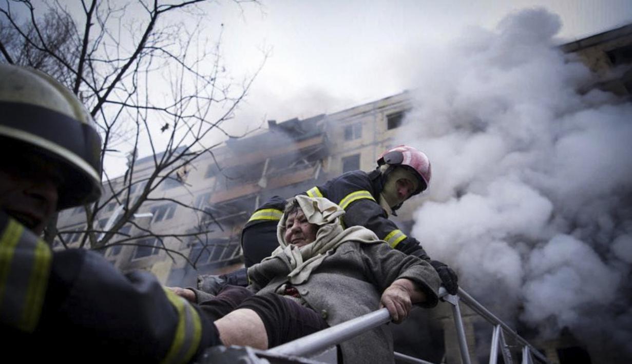 Petugas pemadam kebakaran mengevakuasi seorang wanita tua dari gedung apartemen yang terkena tembakan di Kyiv, Ukraina (14/3/2022). Dua orang tewas pada 14 Maret 2022 akibat serangan penembakan dan rudal Rusia yang menghancurkan gedung apartemen tersebut. (Ukrainian State Emergency Service via AP)