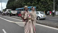 Sepasang pengantin Sri Lanka berjalan menyusuri jalan utama di pusat kota Kandy, 22 September 2017. Pasangan itu membuat kontroversi karena menggunakan sekitar 250 siswa untuk memegang saree atau gaun pengantin wanita India selama pernikahan. (STR/AFP)