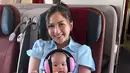 Gaya cantik Jessica Mila duduk di pesawat memangku sang buah hati. Ia tampil chic dengan dress berkerah lengan pendek berwarna biru muda. Kyarra juga tampil menggemaskan engan baju bayi bercorak garis berwarna-warni. [Foto: Instagram/jesicamila03]