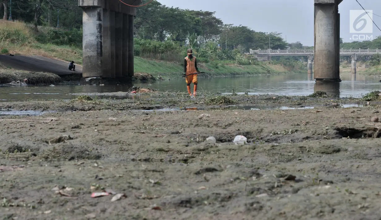 Petugas UPK Badan Air Dinas Lingkungan Hidup Provinsi DKI Jakarta membersihkan rerumputan dan sampah di dasar aliran Kanal Banjir Timur, Jakarta, Rabu (7/8/2019). Kemarau berkepanjangan mengakibatkan debit air Kanal Banjir Timur menyusut hingga dasar aliran terlihat. (merdeka.com/Iqbal Nugroho)