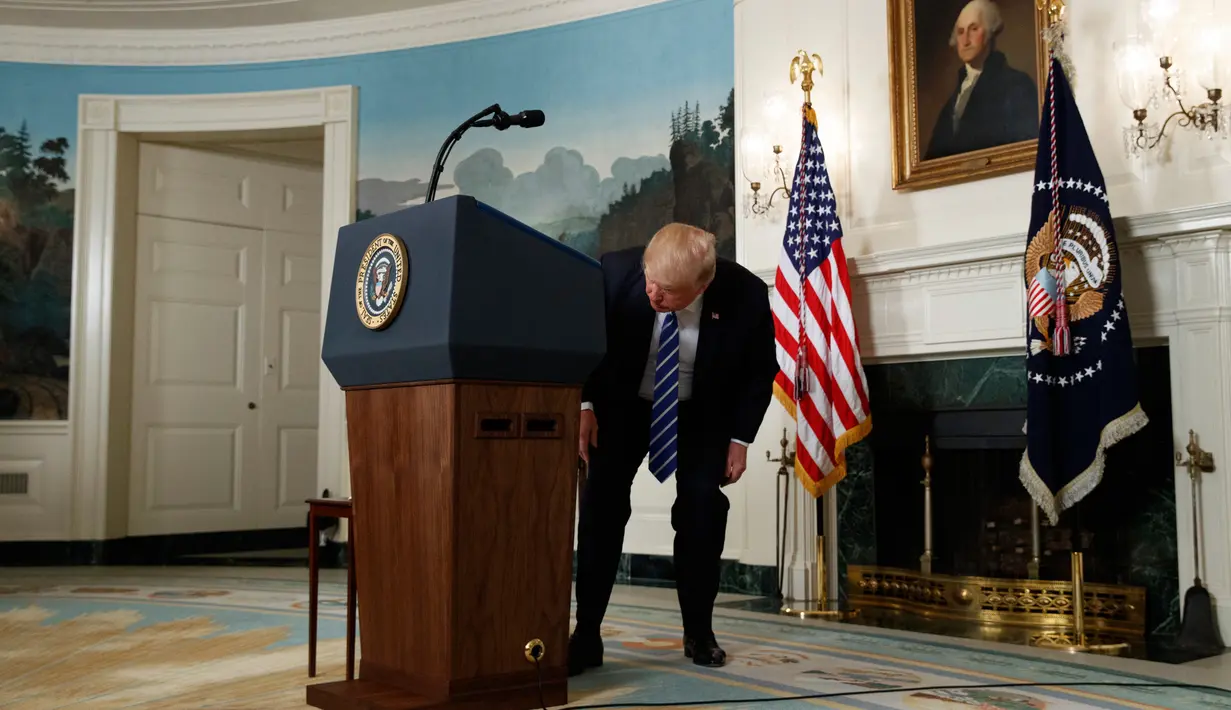 Presiden AS, Donald Trump mencari botol air minum dekat podium disela pidatonya di Ruang Diplomatik, Gedung Putih, Rabu (15/11). Di tengah pemaparan, Trump tiba-tiba terlihat seperti tenggorokannya terganggu dan diduga mengalami dahaga. (AP/Evan Vucci)