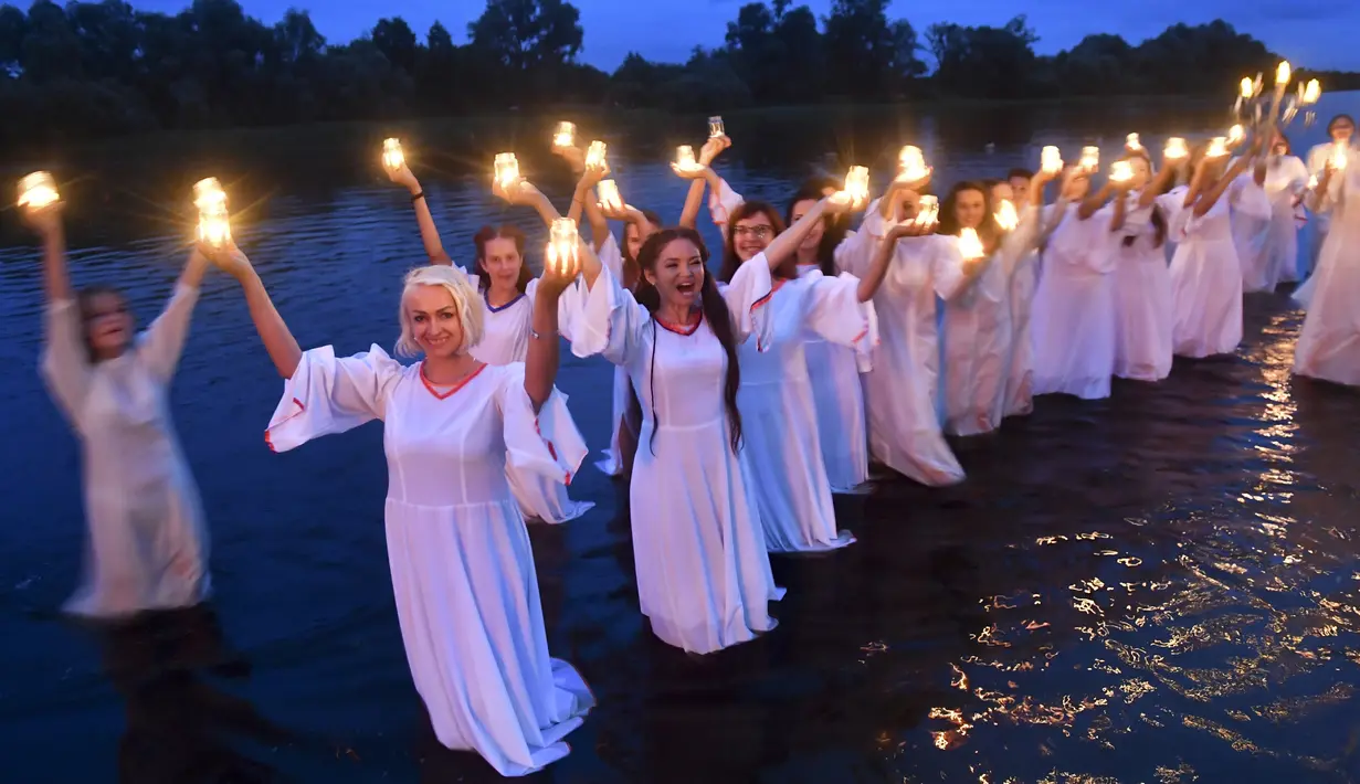 Gadis-gadis Belarusia memegang lilin saat berdiri di Sungai Berezina pada Hari Ivan Kupala di Desa Parichi, sekitar 200 km (125 mil) selatan Parichi, Belarusia, 6 Juli 2022. Ivan Kupala atau Hari St. John atau Hari Pertengahan Musim Panas adalah karnaval tradisional yang berpusat di sekitar api unggun dengan banyak makanan dan tarian. (AP Photo/Viktor Drachev)