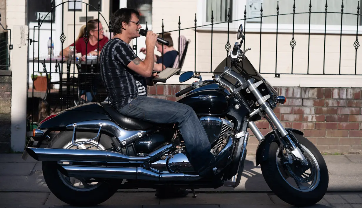 David Walsh dari Dovercliff Road duduk di atas motornya sembari membacakan angka-angka saat penduduk mengikuti permainan Bingo untuk menghibur diri di Liverpool, Inggris, 2 Mei 2020. Selama mengikuti permainan, peserta tetap mematuhi pedoman pemerintah dan menerapkan jaga jarak. (Xinhua/Jon Super)