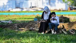 Bagi masyarakat Aceh, momen peringatan tragedi tsunami kali ini bukan hanya mengenang kehilangan masa lalu, tetapi juga tentang menghadapi tantangan masa kini. Tampak dalam foto, seorang wanita dan anaknya membaca Al-Quran sambil berdoa untuk kerabat yang meninggal dunia dalam peristiwa gempa dan tsunami Aceh pada 2004 lalu di sebuah kuburan massal di Siron, pada 26 Desember 2025. (CHAIDEER MAHYUDDIN/AFP)