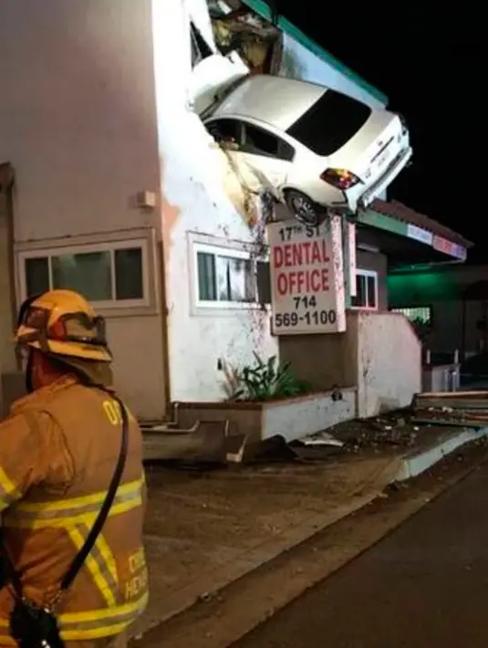 Pemandangan aneh sebuah mobil yang tertancap di bangunan lantai dua klinik dokter gigi di Santa Ana, California, Minggu (14/1). Pihak kepolisian setempat meyakini pengemudi mobil itu terpengaruh atau mabuk narkotika. (Orange County Fire Authority via AP)