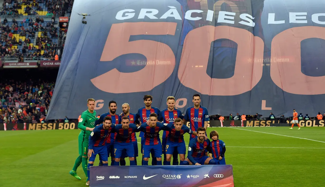 Pemain Barcelona berpose dengan latar belakang spanduk besar penghormatan untuk Lionel Messi yang telah mencetak 500 gol untuk klubnya sebelum pertandingan liga Spanyol antara Barcelona vs Osasuna di stadion Camp Nou, Barcelona (26/4). (AFP/Lluis Gene)