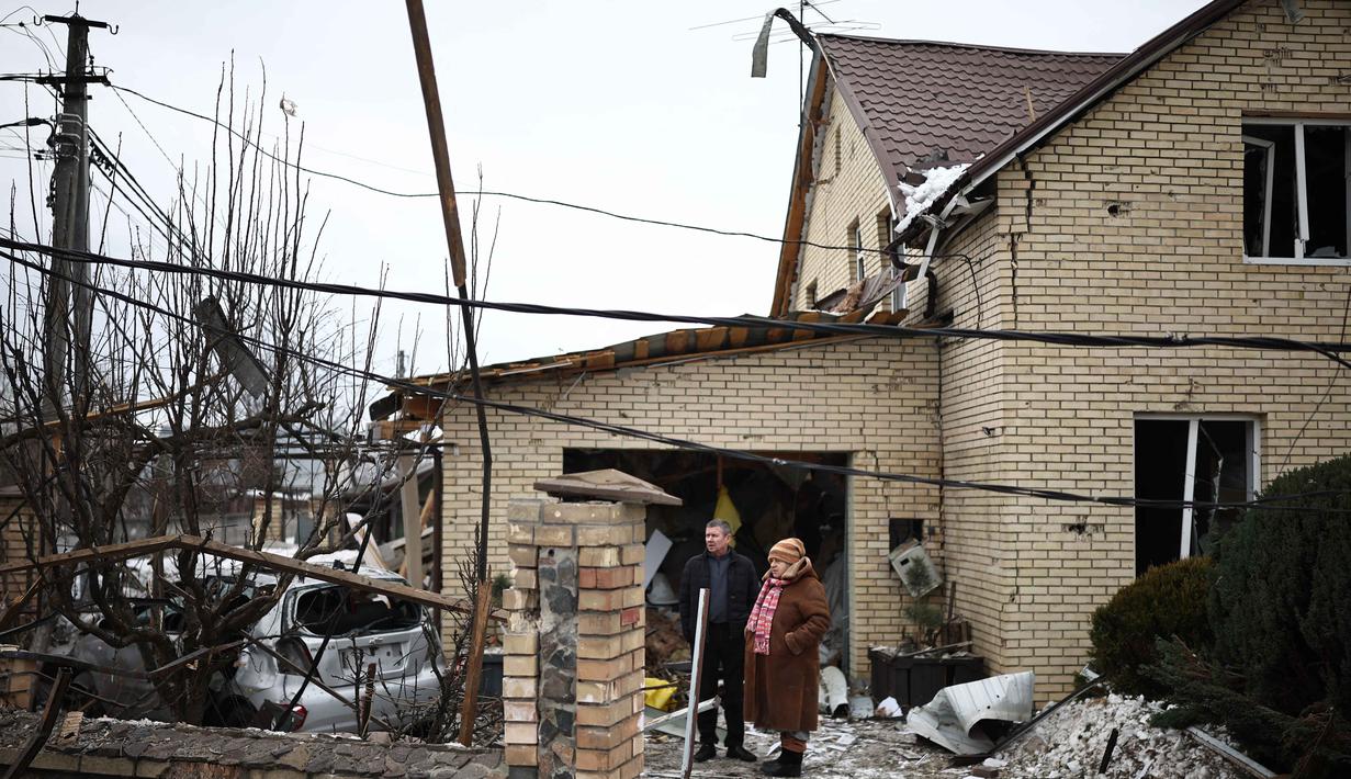 Serangan menyebabkan kerusakan parah di beberapa lokasi. Tampak dalam foto, warga setempat berdiri di antara puing-puing di halaman rumah yang rusak akibat serangan udara di Sofiivska Borshchagivka, wilayah Kyiv pada Minggu 22 Februari 2026. (Henry NICHOLLS/AFP)