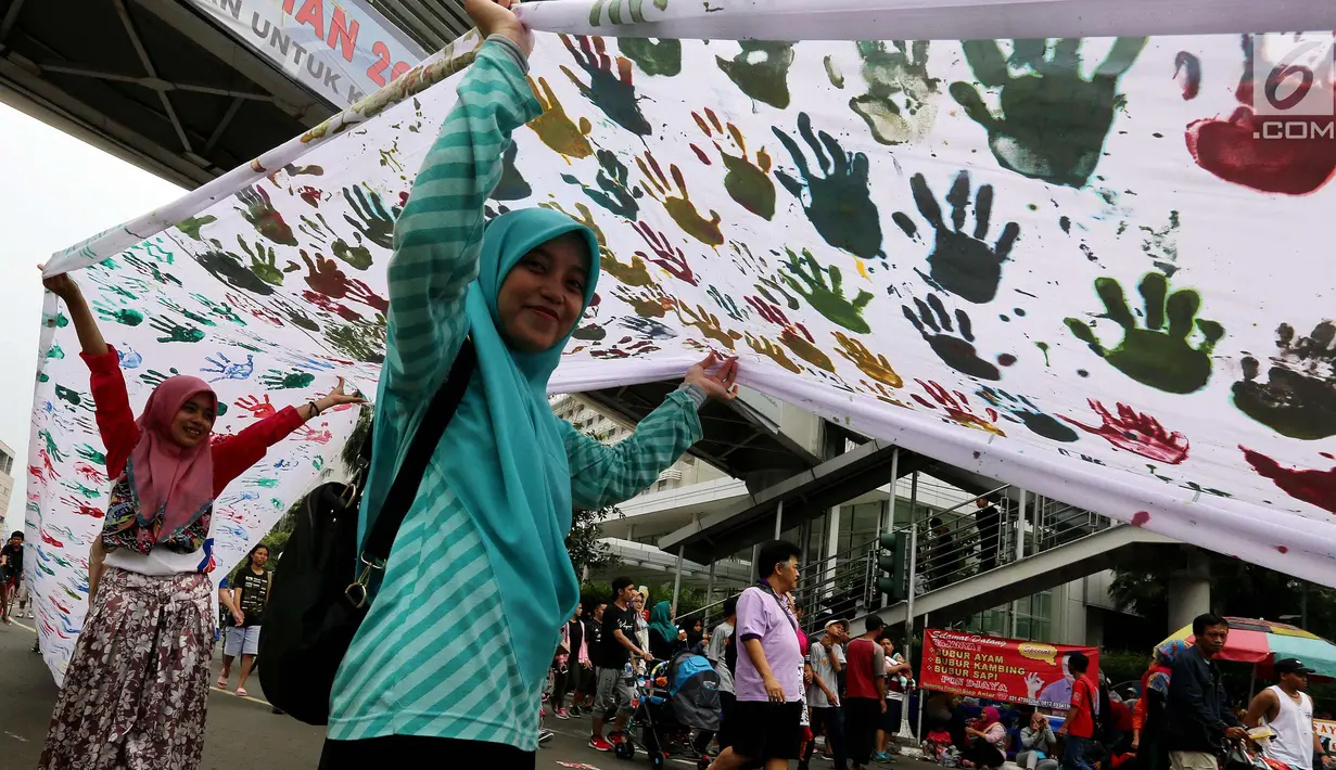 Warga memegang spanduk sepanjang satu kilometer bekas Cap tangan anak-anak Indonesia, di Kawasan Car Free Day, Bundaran HI, Jakarta (24/9). Spanduk tersebut untuk menunjukkan dukungan kepada Etnis minoritas Rohingya di Myanmar. (Liputan6.com/Johan Tallo)