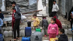 Risiko ini dampak fisik dan psikologis serta penghancuran sekolah yang disebabkan perang selama lebih dari dua tahun. Tampak dalam foto, orang-orang, termasuk anak-anak mengantre untuk mengisi wadah dengan air dari tangki portabel, di kamp pengungsi Palestina Nuseirat di utara Deir al-Balah, Jalur Gaza tengah pada 29 Januari 2026. (EYAD BABA/AFP)